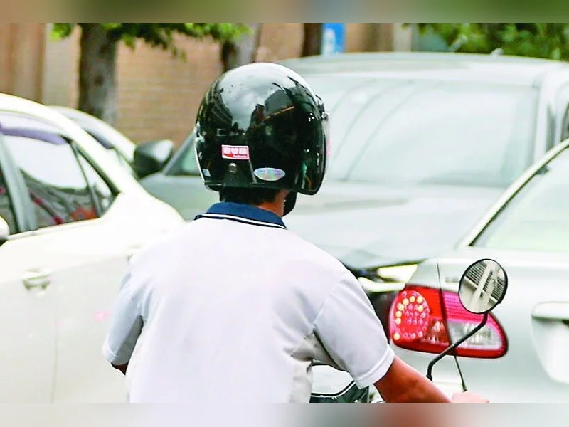 一名戴黑色安全帽、穿白色上衣的騎士在車陣中騎車的背影
