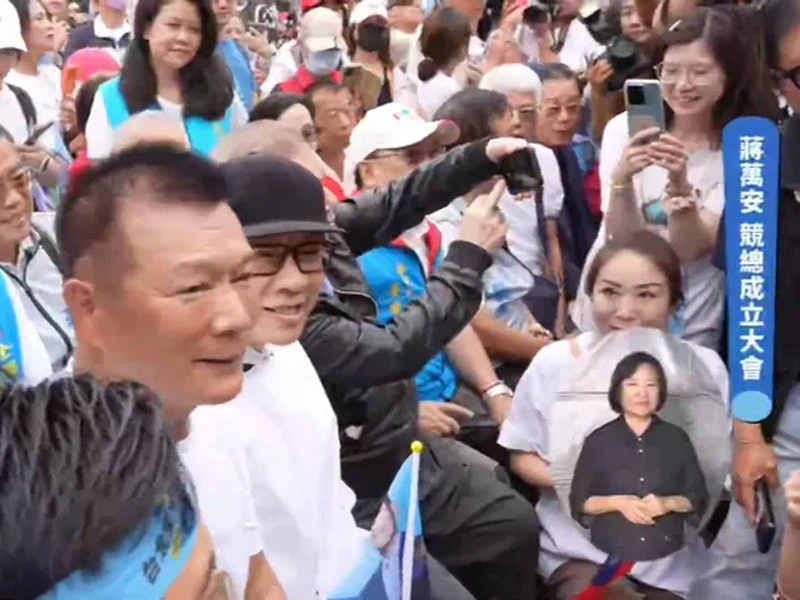蔡康永戴黑帽坐在蔣萬安競總前排，四周支持者拿著手機拍他