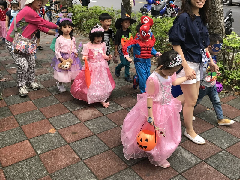 台北松山區街頭，幼兒園小朋友穿著粉紅色公主裙、蜘蛛人裝，提著南瓜桶參加萬聖節遊行