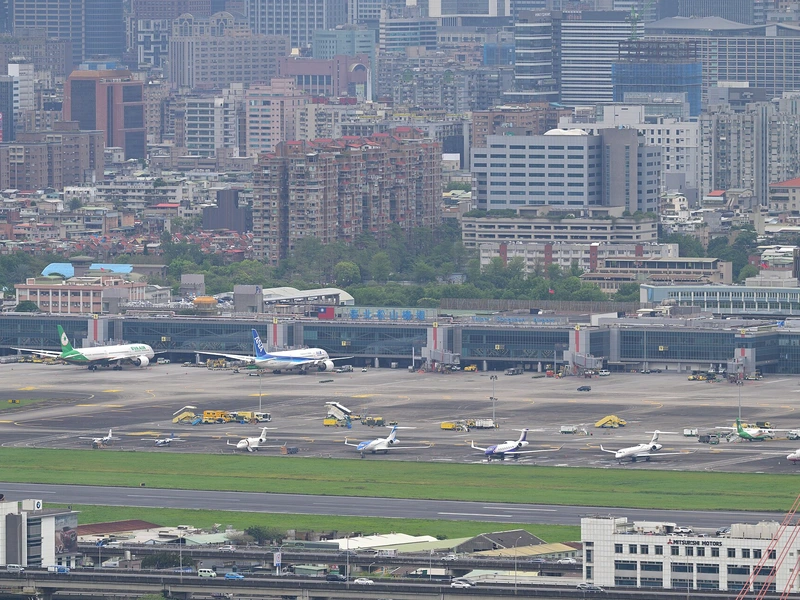 從高處望向松山機場，停機坪上有長榮、全日空等客機，後方是密集的台北市區大樓