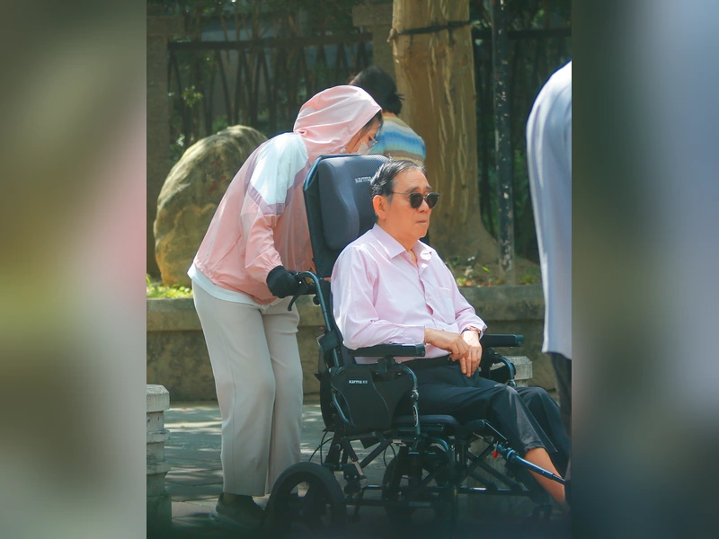 王文洋坐在輪椅上由幫傭推行